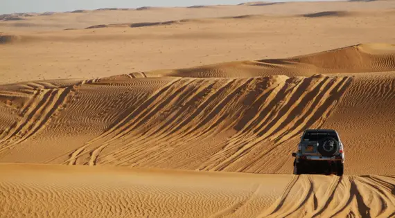 Véhicule tout-terrain 4x4 traversant les dunes de sable du Sahara à Dakhla pour une session de kitesurf sauvage.